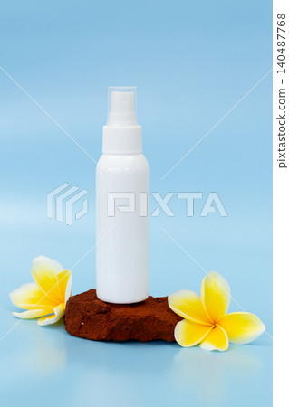 White spray bottle rests on brown stone. Two yellow frangipani flowers frame the scene. Soft blue background adds calming atmosphere. Minimalist setup highlights product elegance. Ideal for skincare White spray bottle rests on brown stone. Two yellow frangipani flowers frame the scene. Soft blue background adds calming atmosphere. Minimalist setup highlights product elegance. Ideal for skincare 140487768