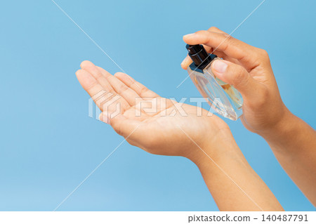 Hands spray sanitizer onto open palm. Blue background provides clean contrast. Hygiene and safety concept visually emphasized. Image conveys care and preparedness during pandemic times 140487791