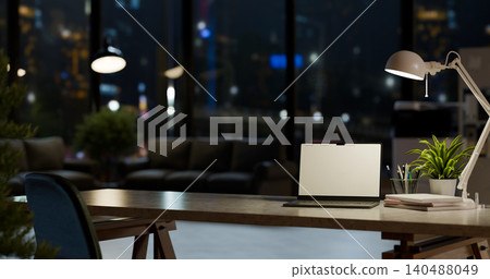 Night office desk with laptop cocmputer lamp, books and plant, city lights background Night office desk with laptop cocmputer lamp, books and plant, city lights background 140488049