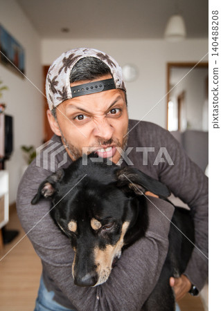 A man is hugging a black dog with a hat on his head A man is hugging a black dog with a hat on his head 140488208