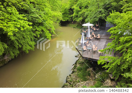 Scenic river terrace features modern patio seating with umbrellas and glass railings Scenic river terrace features modern patio seating with umbrellas and glass railings 140488342