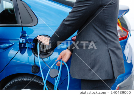 The driver of the electric car inserts the electrical connector to charge the batteries. Unrecognizable man attaching power cable to electric car. 140489000