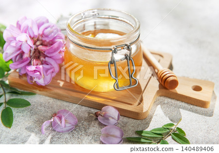 Acacia honey jar with blooming flowers and wooden dipper Acacia honey jar with blooming flowers and wooden dipper 140489406