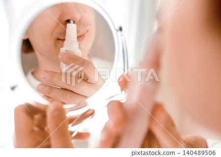 A man uses an electric trimmer for nose hair removal while looking in a mirror. Daily male hygiene, facial care, and grooming routine. A man uses an electric trimmer for nose hair removal while looking in a mirror. Daily male hygiene, facial care, and grooming routine. 140489506