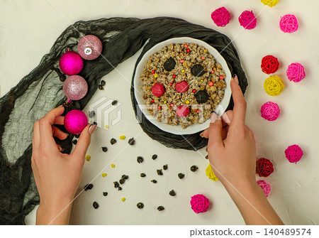 Modern ukrainian christmas kutia in white bowl held by woman's hands with colorful berries, candy pearls, and decorative balls on white background. Modern ukrainian christmas kutia in white bowl held by woman's hands with colorful berries, candy pearls, and decorative balls on white background. 140489574