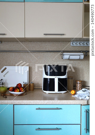 Trendy kitchen gadget modern white air fryer on a kitchen countertop machine cooking deep-fried. Minimalist kitchen background with accessories. Lifestyle of new cooking. Trendy kitchen gadget modern white air fryer on a kitchen countertop machine cooking deep-fried. Minimalist kitchen background with accessories. Lifestyle of new cooking. 140490773