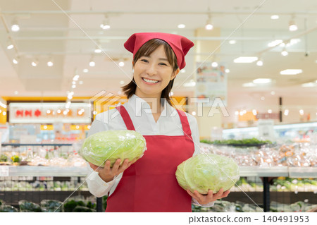 A female supermarket employee smiles while holding a cabbage. A female supermarket employee smiles while holding a cabbage. 140491953