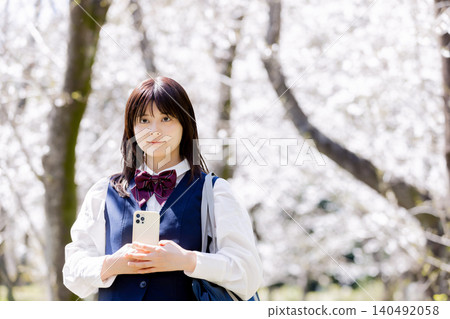 A spring portrait of a high school girl holding a smartphone under a row of cherry trees. A spring portrait of a high school girl holding a smartphone under a row of cherry trees. 140492058