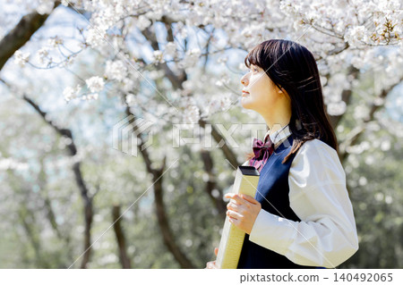 A high school girl looks towards the future, holding her graduation certificate under the fully bloomed cherry blossoms. A high school girl looks towards the future, holding her graduation certificate under the fully bloomed cherry blossoms. 140492065