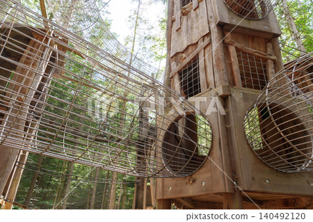 Wooden tower and mesh tunnels in forest adventure park 140492120