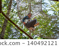 Child sitting inside mesh tunnel in forest adventure park 140492121