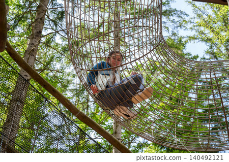 Child sitting inside mesh tunnel in forest adventure park Child sitting inside mesh tunnel in forest adventure park 140492121