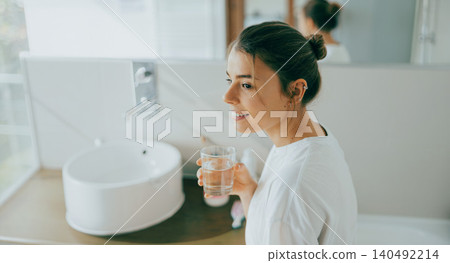 Happy young Caucasian woman holding a glass of water in a bright modern bathroom Happy young Caucasian woman holding a glass of water in a bright modern bathroom 140492214