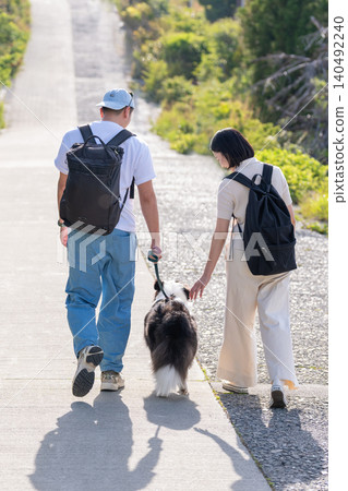 A couple enjoying a trip with their dog, seen from behind. 140492240