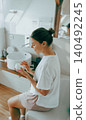 Caucasian young adult woman applying moisturizing cream while sitting in a modern bathroom 140492245