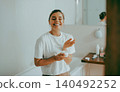Happy young Caucasian woman applying skin cream while smiling in a bright bathroom 140492252