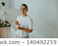 Happy Caucasian young adult woman smiling and holding cosmetic cream jar in a bright bathroom 140492259