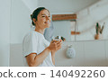 Happy young Caucasian woman smiling while holding a glass of fresh water in a bright bathroom 140492260
