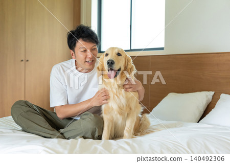 A man interacting with a golden retriever on a bed. A man interacting with a golden retriever on a bed. 140492306