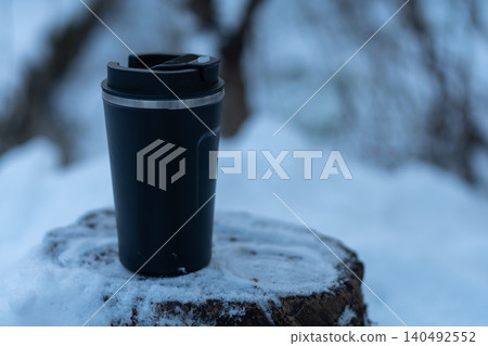 A hot drink in a thermal mug amidst a snowy forest setting. A hot drink in a thermal mug amidst a snowy forest setting. 140492552
