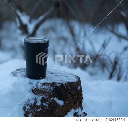 A thermos mug against a snowy winter backdrop. A thermos mug against a snowy winter backdrop. 140492554