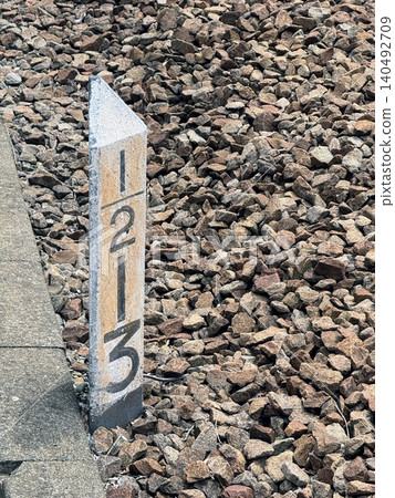 A railway kilometer post and numbers stand amidst the gravel beside the tracks. A railway kilometer post and numbers stand amidst the gravel beside the tracks. 140492709