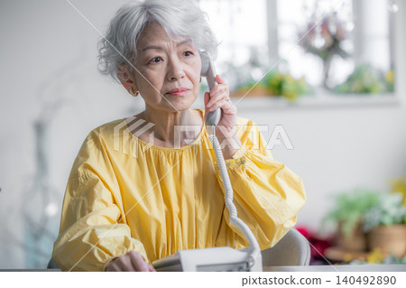 A senior woman making a phone call on a landline. A senior woman making a phone call on a landline. 140492890