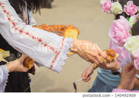 Bread is shared by woman in folk costume with children during village festival ceremony outdoors. Folk tradition, hospitality, culture, celebration, family ritual, food concept Bread is shared by woman in folk costume with children during village festival ceremony outdoors. Folk tradition, hospitality, culture, celebration, family ritual, food concept 140492989