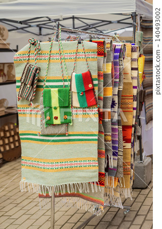 Woven rugs and bags hang on market rack, outdoor bulgarian craft stall with textile products. Woven textile, souvenir shopping, heritage craft, tourism, folk design, home decor retail Woven rugs and bags hang on market rack, outdoor bulgarian craft stall with textile products. Woven textile, souvenir shopping, heritage craft, tourism, folk design, home decor retail 140493002