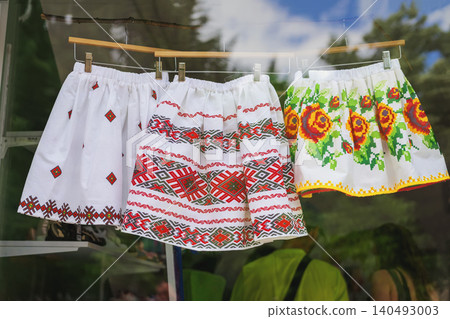 Embroidered skirts with Bulgarian folk patterns hang in shop window as souvenir clothing display. Bulgarian textile supports heritage craft, retail market, tourism, folk fashion Embroidered skirts with Bulgarian folk patterns hang in shop window as souvenir clothing display. Bulgarian textile supports heritage craft, retail market, tourism, folk fashion 140493003