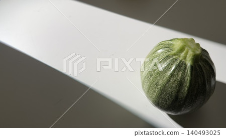 圓形的西葫蘆擺放在白色桌子上,沐浴在自然光中。 圓形的西葫蘆擺放在白色桌子上,沐浴在自然光中。 140493025