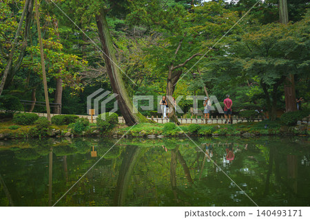 Kanazawa, Japan - Oct 6 2024, panoramic view of the mirror-like pond in Kenroku-en Park, with people strolling along the coastline in the background, at daytime, Kanazawa, Japan  140493171