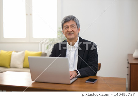 A man in his 60s wearing a jacket working on a laptop. A man in his 60s wearing a jacket working on a laptop. 140493757