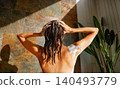Caucasian young adult woman washing hair with shampoo in modern natural stone bathroom 140493779
