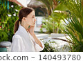 Young Caucasian woman in bathrobe touching face looking aside in green botanical spa resort 140493780