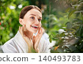 Happy young Caucasian woman smiling while doing skincare routine in bright green spa 140493783