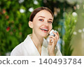 Happy young Caucasian woman holding a facial cleansing brush in a bright green bathroom 140493784