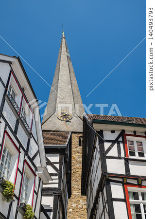 Church clock tower with steeple in Germany, historic old town architecture low angle view, traditional half timbered houses against blue sky in medieval european village Church clock tower with steeple in Germany, historic old town architecture low angle view, traditional half timbered houses against blue sky in medieval european village 140493793