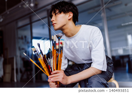 一位年輕藝術家在他的工作室裡拿著畫筆。 一位年輕藝術家在他的工作室裡拿著畫筆。 140493851