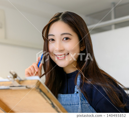 一位微笑的女學生正在藝術預科學校畫畫。 一位微笑的女學生正在藝術預科學校畫畫。 140493852