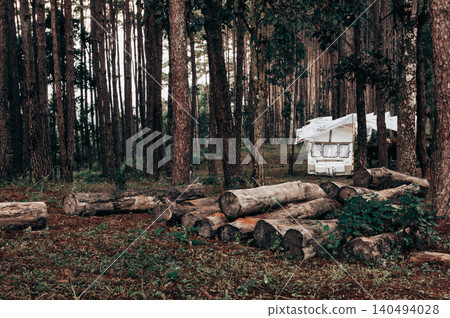 Group of white RVs are parked in a forest. The scene is dark and moody, with the trees casting shadows on the ground. The RVs are all facing the same direction, creating a sense of unity. Group of white RVs are parked in a forest. The scene is dark and moody, with the trees casting shadows on the ground. The RVs are all facing the same direction, creating a sense of unity. 140494028