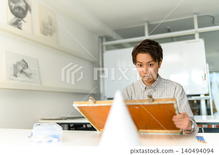 A male student stares at a plaster cast and sketches it. 140494094