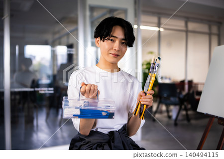 A boy from an art preparatory school carrying a brush and a toolbox. 140494115