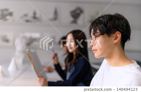 A boy and a girl sketching in an art class. 140494123
