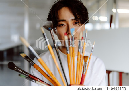 一位來自藝術預科學校的男子,手裡拿著許多畫筆。 一位來自藝術預科學校的男子,手裡拿著許多畫筆。 140494153