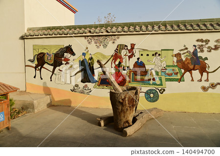 An ancient mortar and pestle by the wall, adorned with paintings depicting life in the Kuche Palace, China. An ancient mortar and pestle by the wall, adorned with paintings depicting life in the Kuche Palace, China. 140494700