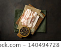 Raw bacon on wooden cutting board on brown background. 140494728