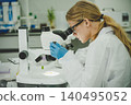Female scientist using microscope to examine sample with focus in advanced research laboratory 140495052