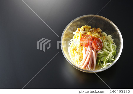 A single serving of chilled ramen in a clear glass bowl, photographed against a black background. A single serving of chilled ramen in a clear glass bowl, photographed against a black background. 140495120