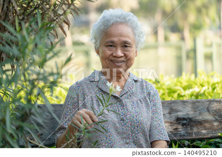 Asian elderly woman sitting on bench with flower to relax in park. Asian elderly woman sitting on bench with flower to relax in park. 140495210